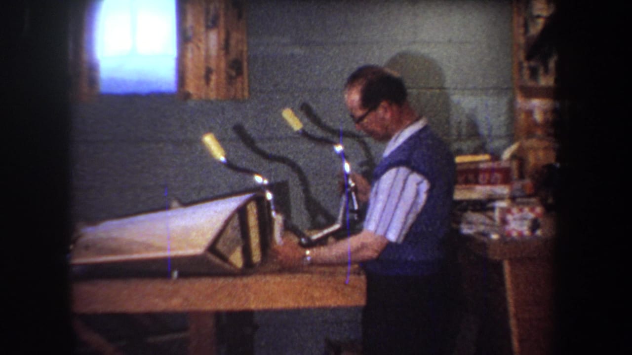 In 1965 Yucaipa home-movie footage, a man in glasses examines a bicycle handlebar area beside a wooden workbench.