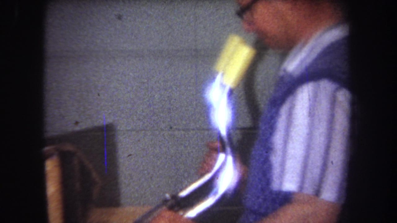 1965 8mm frame from Yucaipa showing a blurred adult man moving inside a workshop-like space before the aircraft frame shots.