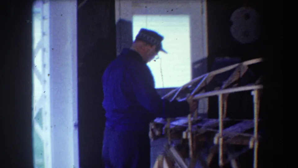 1965 Yucaipa frame showing the man from behind as he examines the wooden structure of a small aircraft under construction.