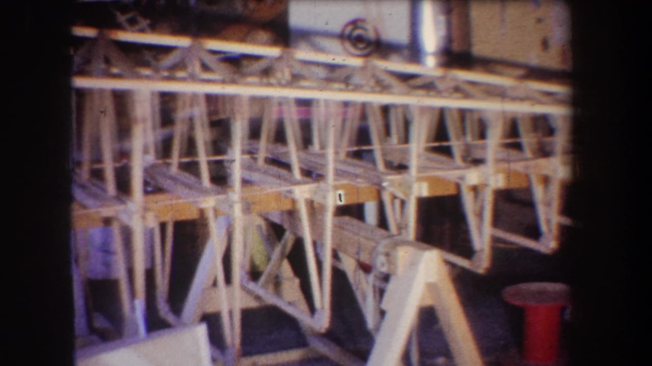 1965 Yucaipa-area home-movie frame showing a light wood aircraft structure under construction in a private workshop.