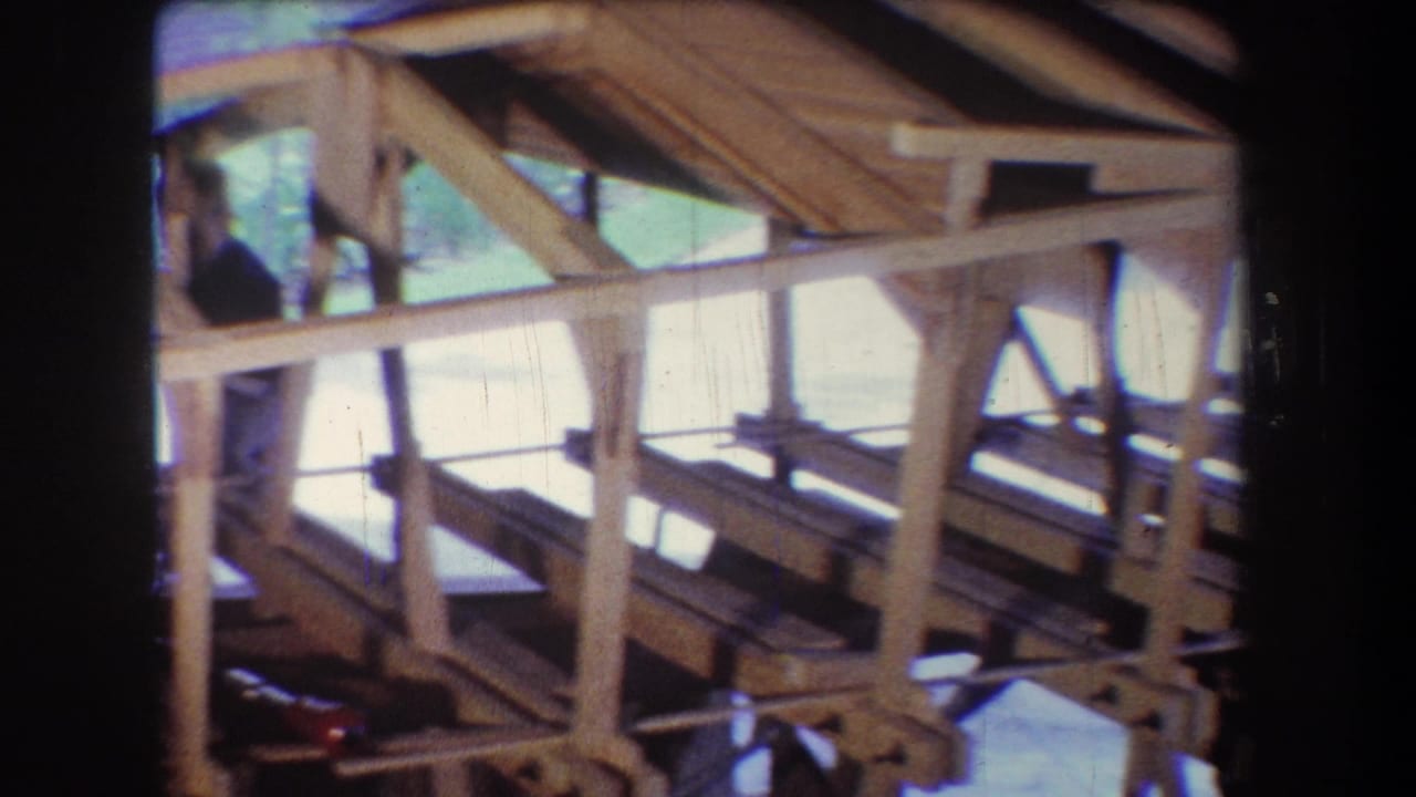 Wooden frame structure with rafters and a worker partly visible near the left side.