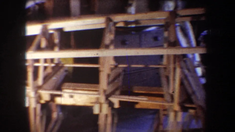 1965 home-movie frame from Yucaipa showing the lower framing of an unfinished wooden structure, with beams, supports, shadowed materials, and soft 8mm color fade.
