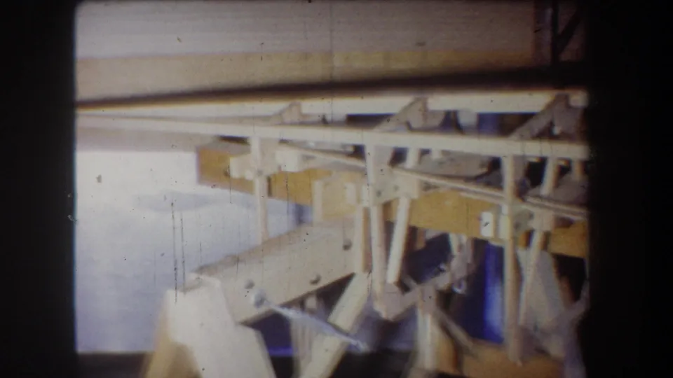 Soft 1965 8mm shot of the wooden boat frame, with bright exposure across the pale beams and visible construction bracing.