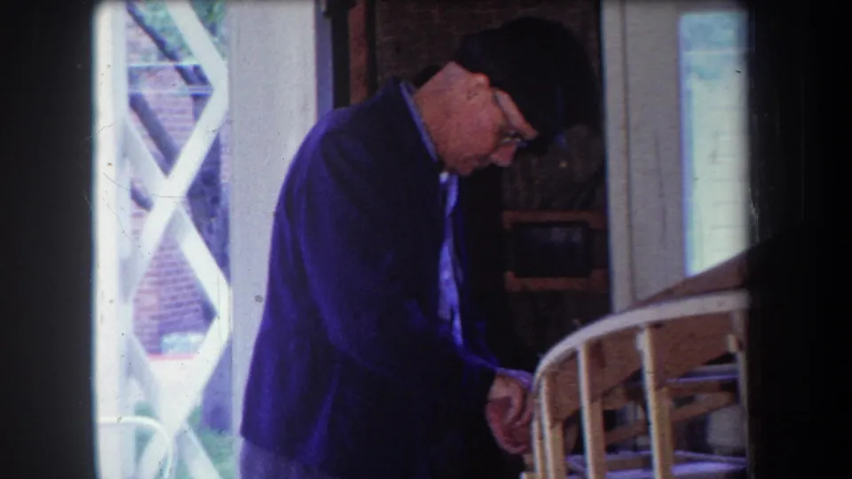 At the end of the clip, the man leans toward the wooden model airplane frame on the residential porch.