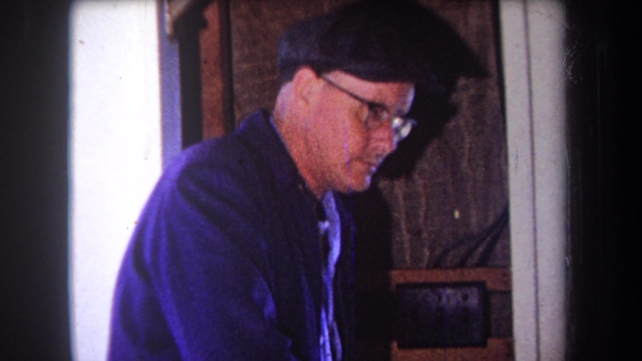 Close view of a man in glasses and a cap working beside wood and workshop walls.