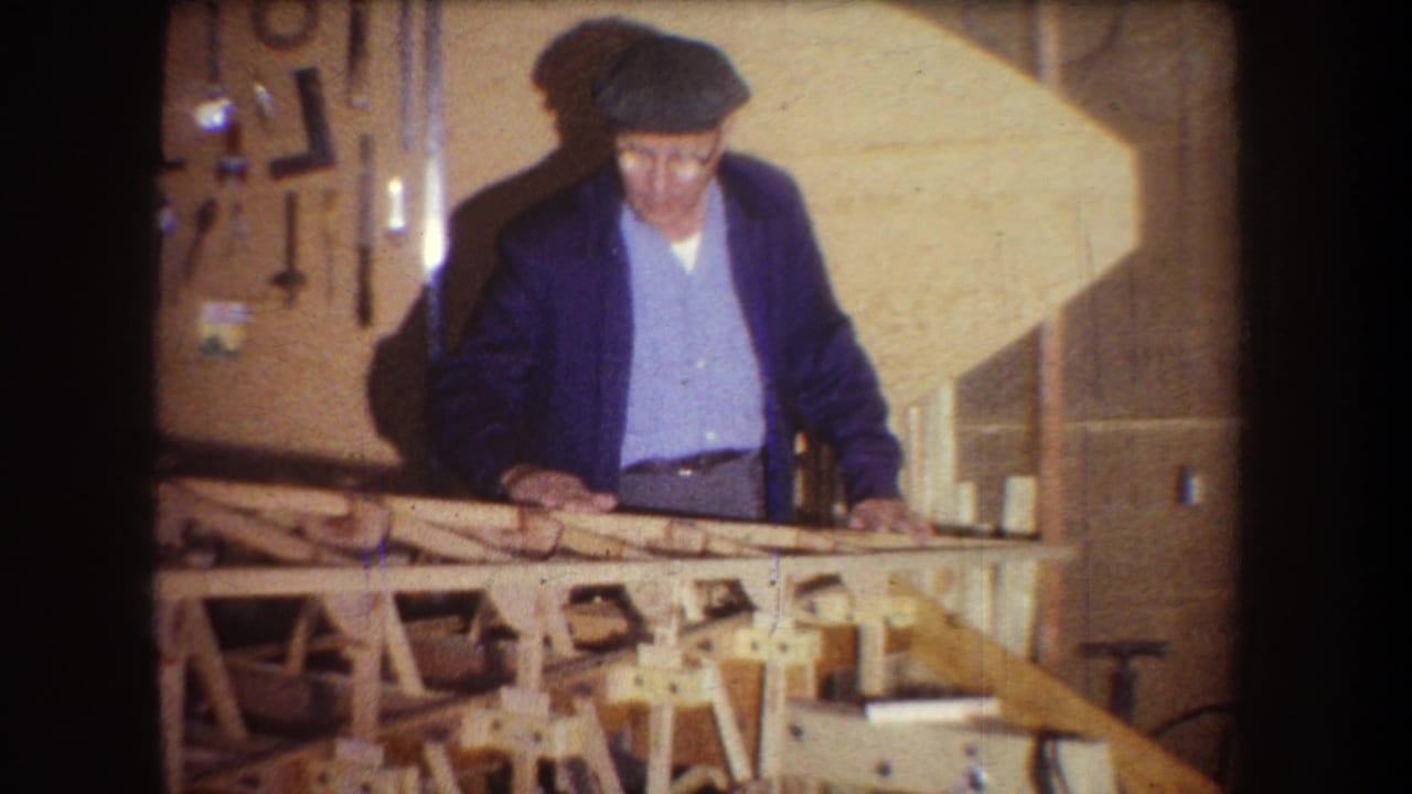 Older man in a blue shirt and dark jacket looks down at a wooden frame inside a Yucaipa workshop.
