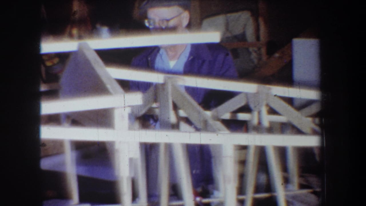 Man stands partly behind a wooden frame with workshop materials around him.