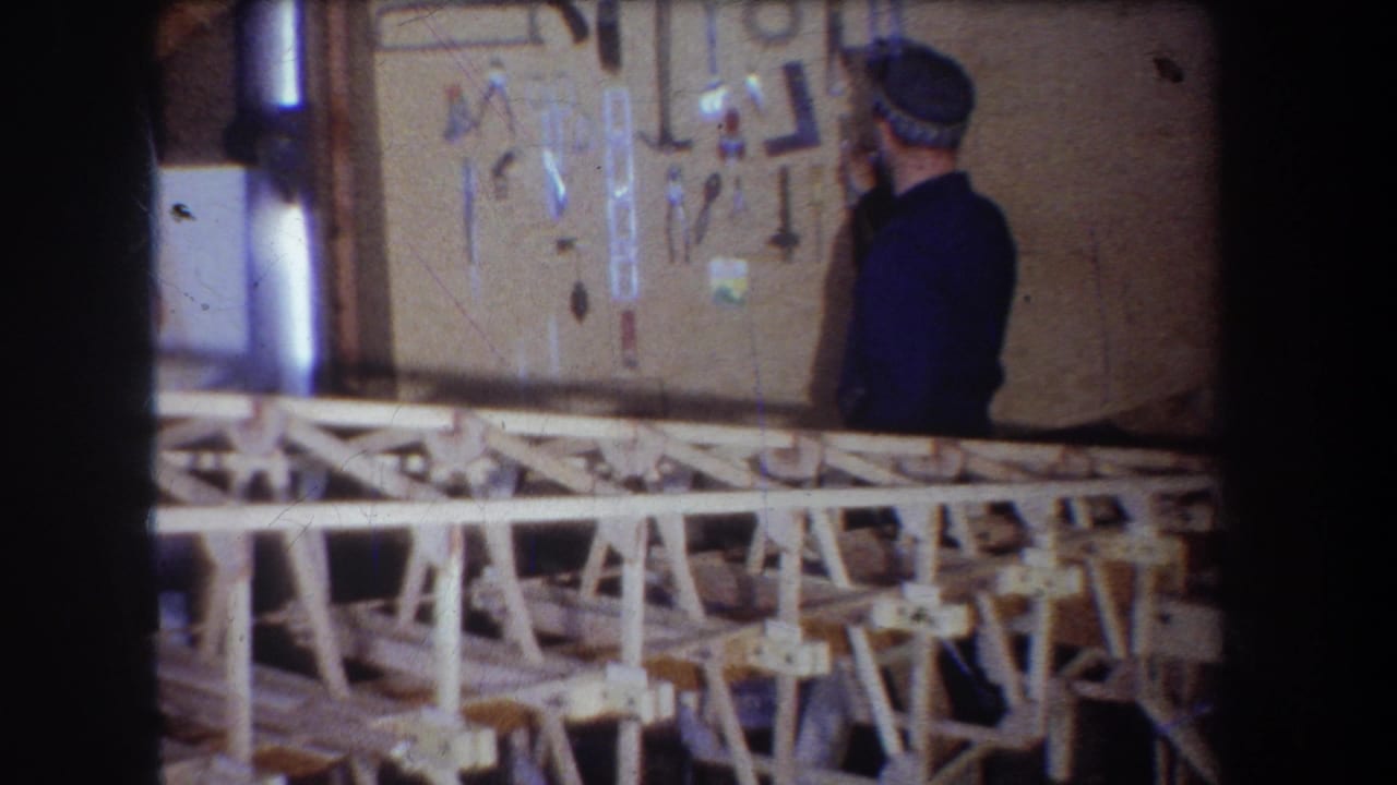 In a 1965 Yucaipa-area workshop scene, a man in a blue jacket and cap faces a wall of hanging tools behind pale wooden benches.