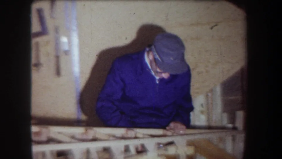 At the end of the clip, the man bends over the bench in the 1965 workshop, partly shadowed against the tool wall.