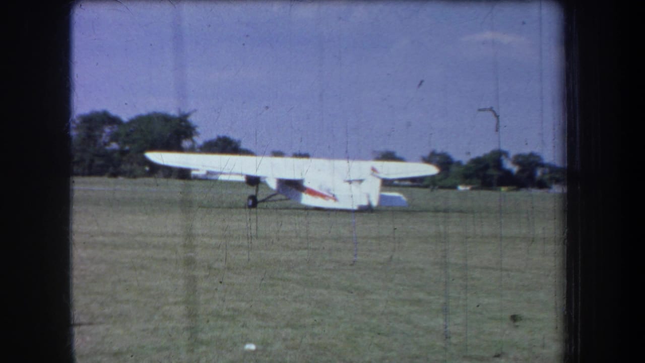 1965 Yucaipa-area 8mm frame showing a white light airplane on a grass airfield with trees in the background.