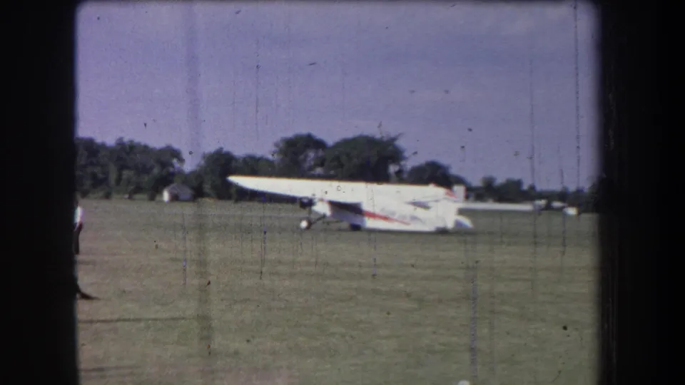 Yucaipa-area 1965 home-movie frame showing a small white aircraft on grass beneath a clear sky.