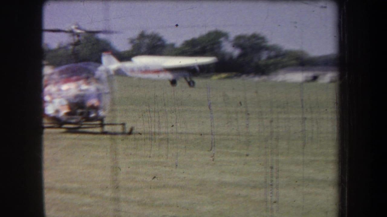 A bubble-canopy helicopter sits in the foreground while a small white airplane moves across the grassy Yucaipa-area airfield.