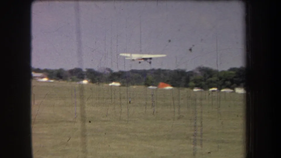 1965 8mm home-movie frame showing the propeller plane gaining height over a rural California grass airfield.