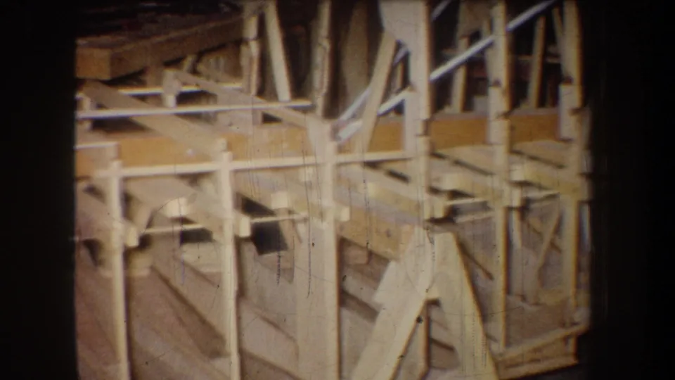 Angled 1965 8mm view of a Yucaipa warehouse interior, emphasizing exposed wooden beams, braces, and construction framing.