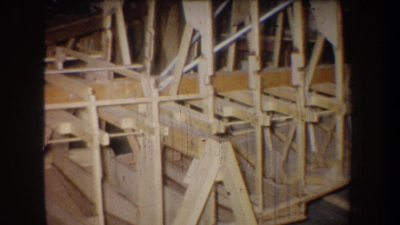 1965 8mm frame from Yucaipa showing a close section of a wooden truss-like assembly with braces, posts, and shop-floor shadows.