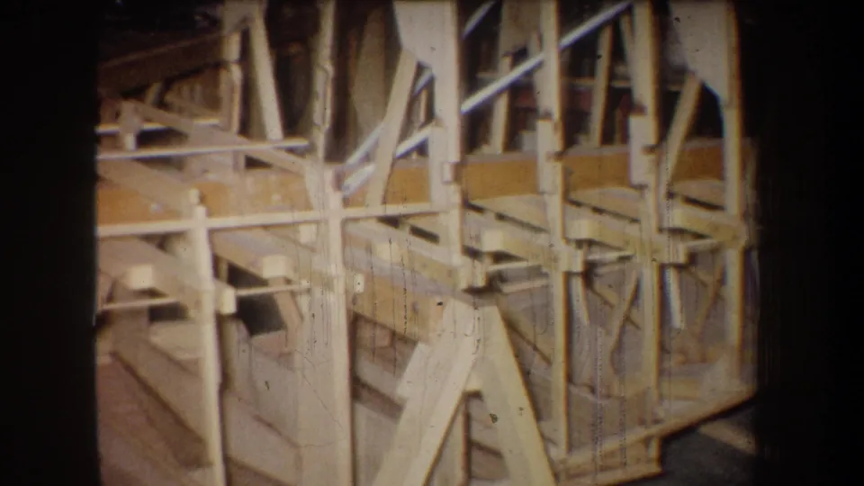 1965 8mm frame from Yucaipa showing a close section of a wooden truss-like assembly with braces, posts, and shop-floor shadows.