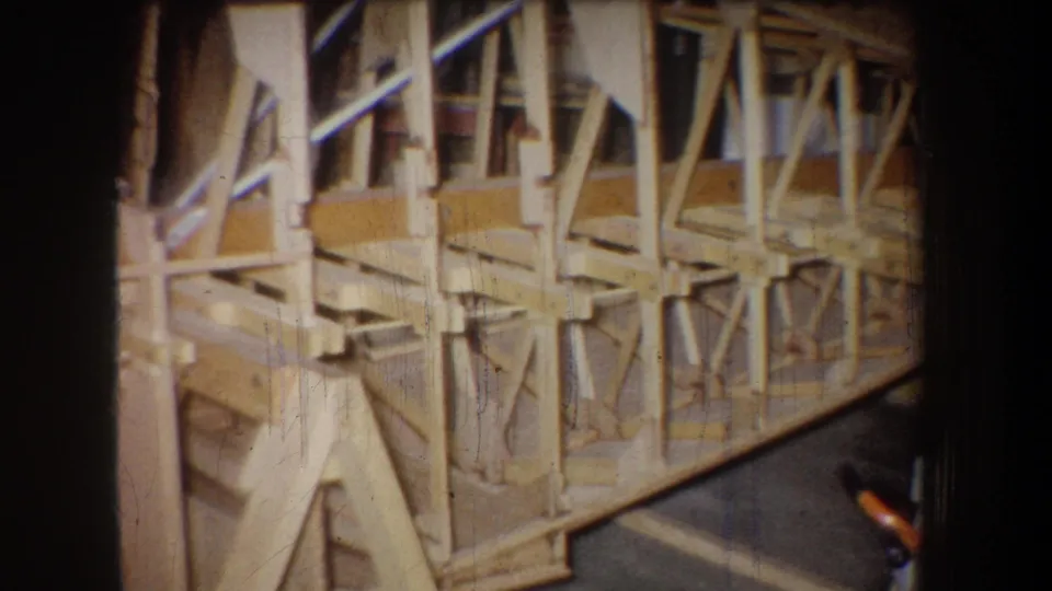 The camera frames an extended wooden structure with repeated braces and rails, likely part of a workshop-built model or assembly.