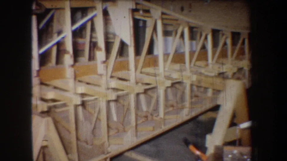 Angled 8mm view of the wooden framework, showing repeated triangular bracing and rails in a workshop setting.