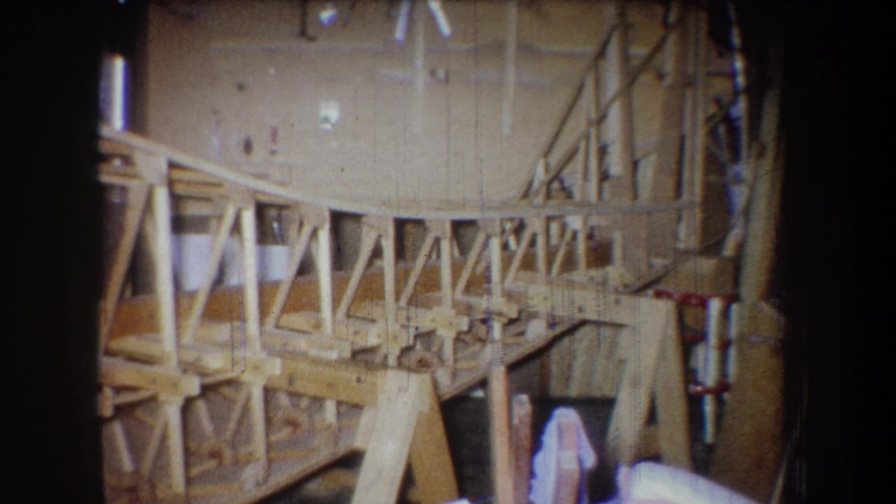 1965 Yucaipa workshop footage showing the wooden framework from a slightly shifted angle, with truss braces and materials around it.