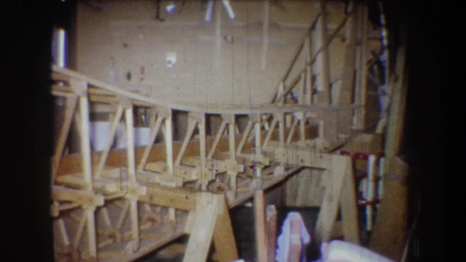 1965 Yucaipa workshop footage showing the wooden framework from a slightly shifted angle, with truss braces and materials around it.