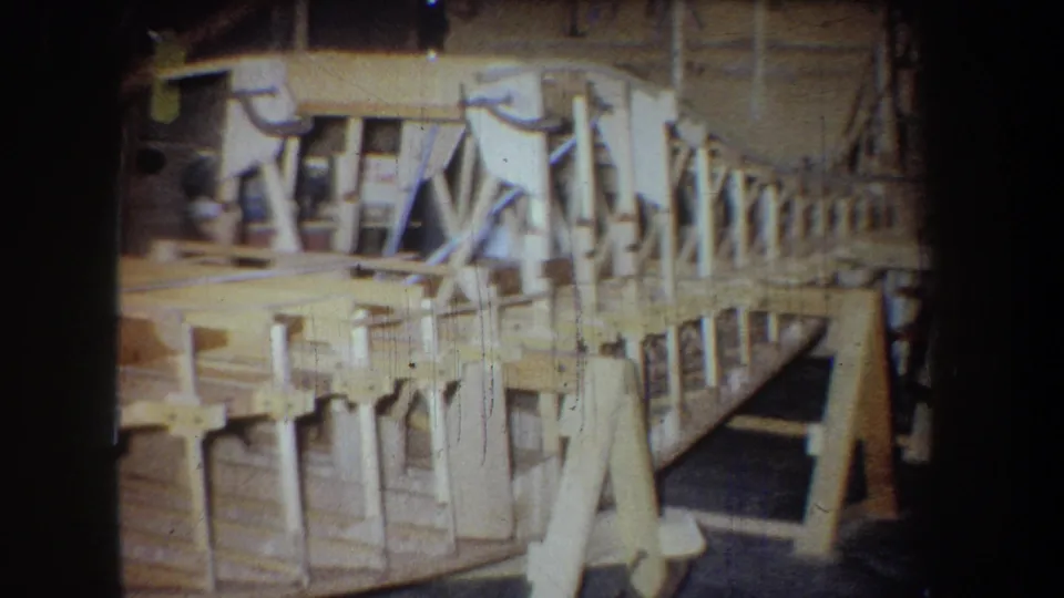 Side view of the wooden aircraft skeleton in a California workshop, with ribs, braces, and support stands visible.