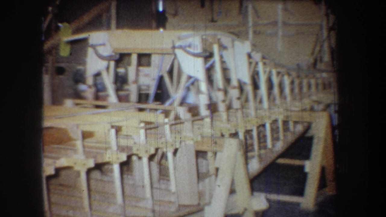 1965 8mm frame from Yucaipa showing a wooden boat hull under construction inside a cluttered workshop.