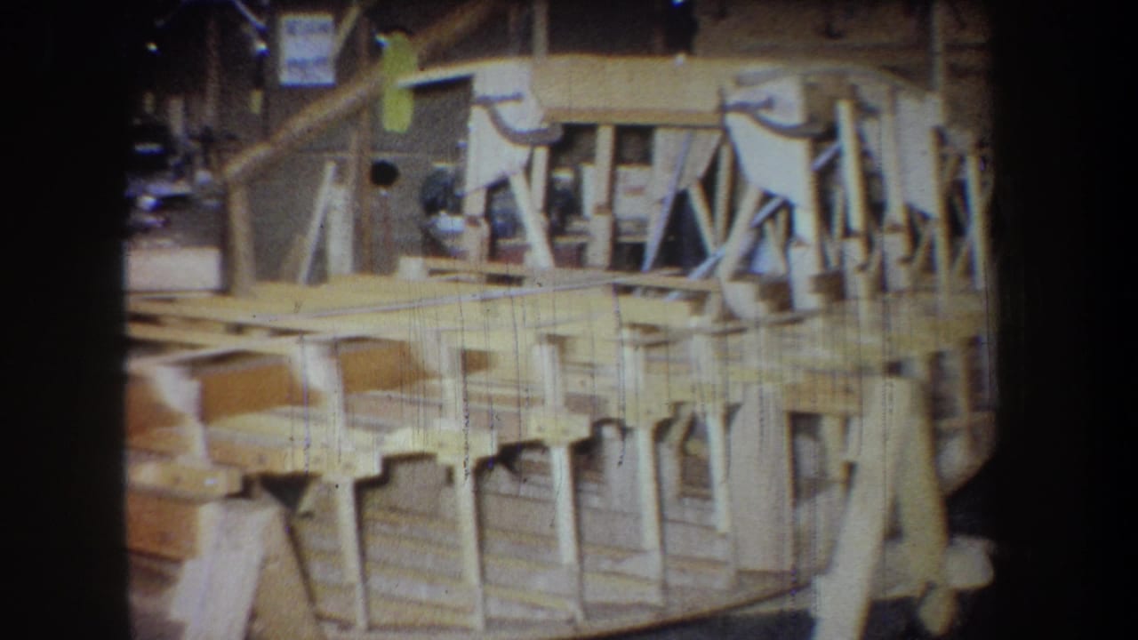 The camera pans across the 1965 Yucaipa workshop, showing the boat hull side, framing members, and support structure.