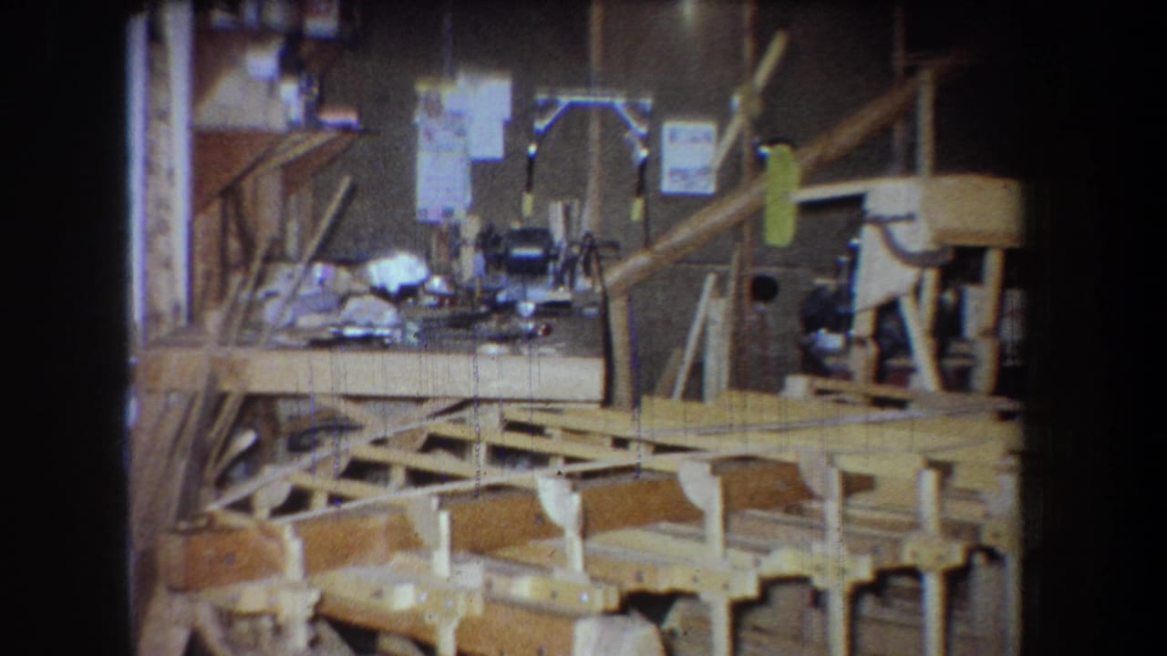 1965 Yucaipa home-movie frame showing a wooden bridge under construction among workbenches, tools, and shop clutter.