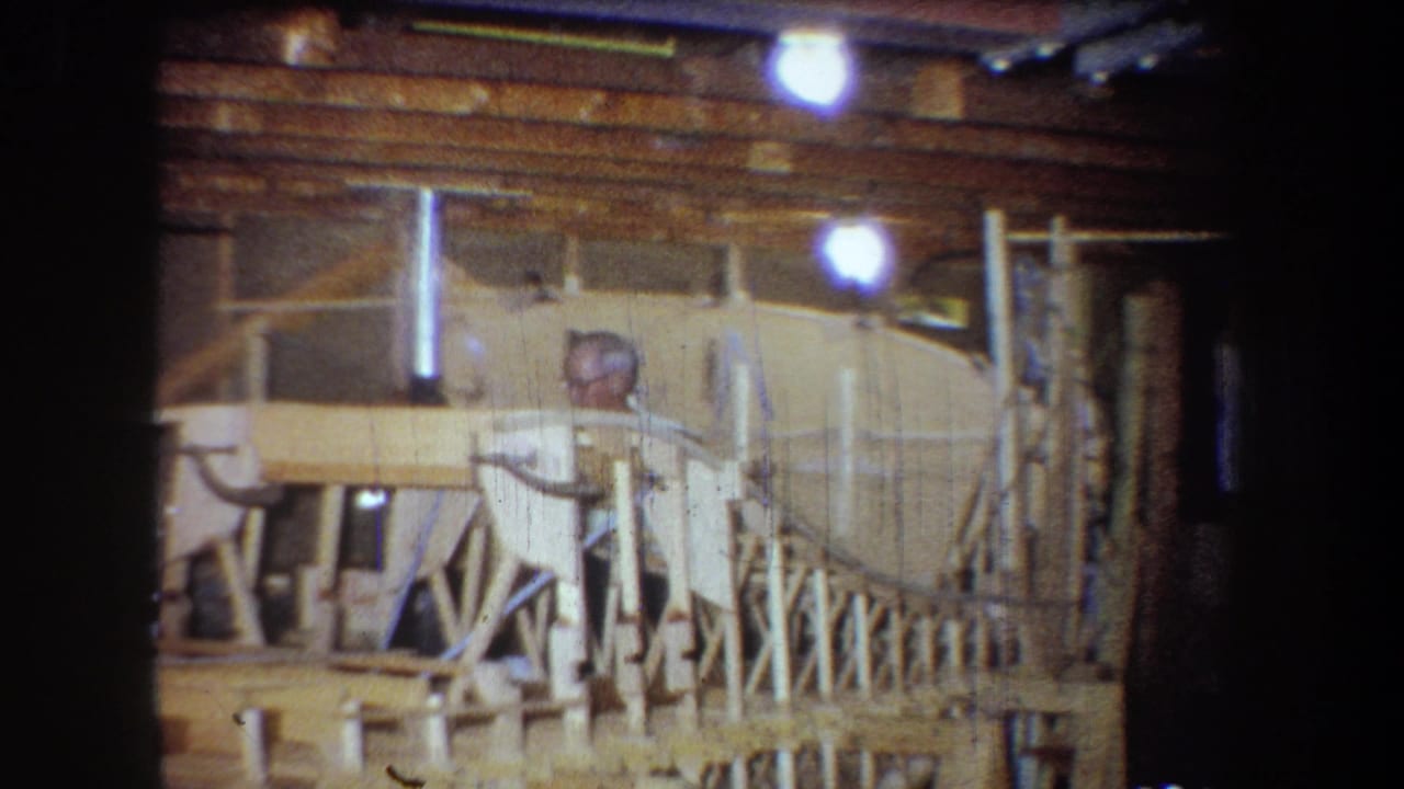 1965 home-movie frame from Yucaipa showing a man with glasses working behind wooden framing in a basement or garage workshop.