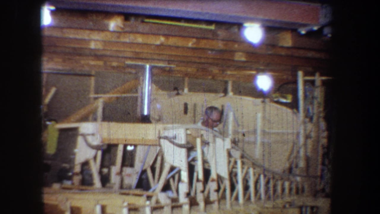 Workshop view with man partly hidden behind wooden supports and a large pale object.