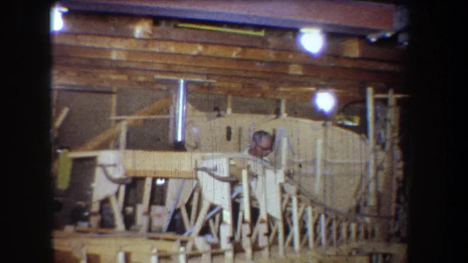 1965 Yucaipa workshop frame with an adult man partly obscured by wood supports, tools, and construction materials.