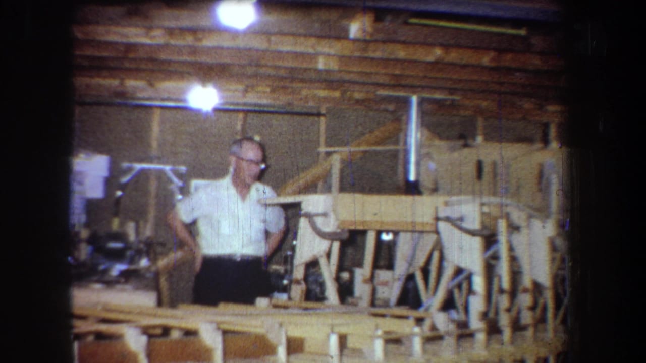 Man in glasses beside wooden boat framing in a workshop interior.