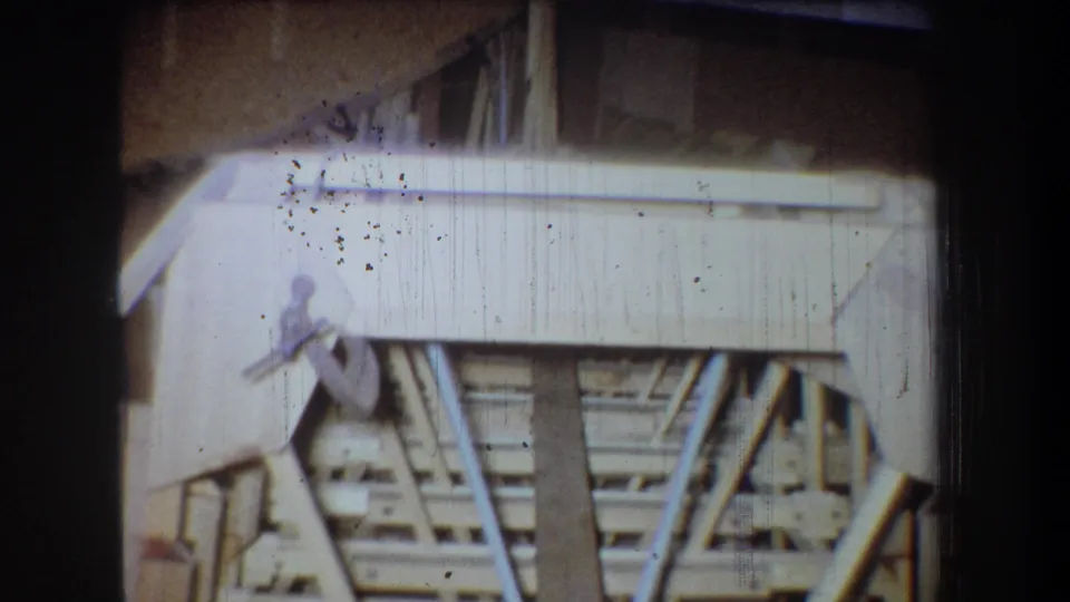 1965 8mm frame from Volmer Yucaipa showing unfinished attic rafters, pale boards, and dark surrounding film edges.