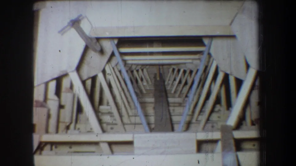 1965 8mm home-movie view inside an unfinished Volmer Yucaipa attic, with rafters and beams receding into shadow.