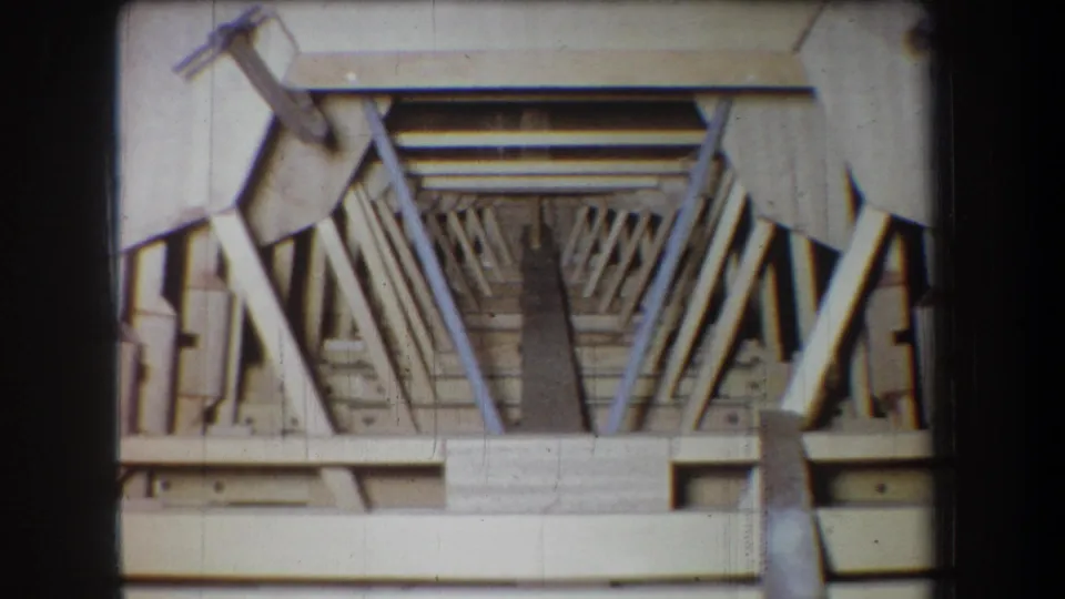 1965 home-movie still showing the same wooden model or framework, with pale beams converging toward a dark center.
