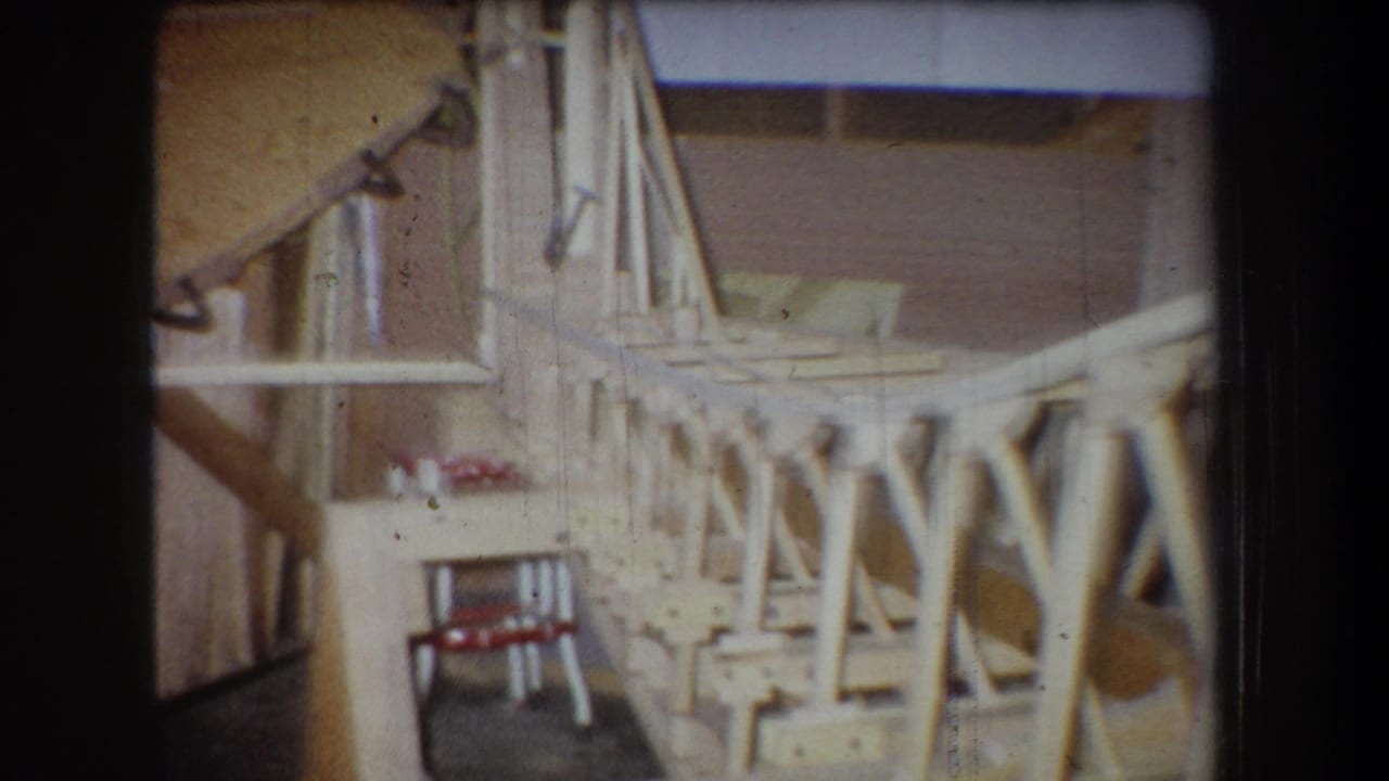 1965 Yucaipa home-movie frame showing a side section of unfinished wooden airplane framing inside a workshop-like space.