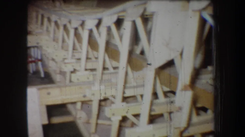 1965 home-movie view of the unfinished wooden aircraft structure, focusing on side trusses and diagonal bracing.