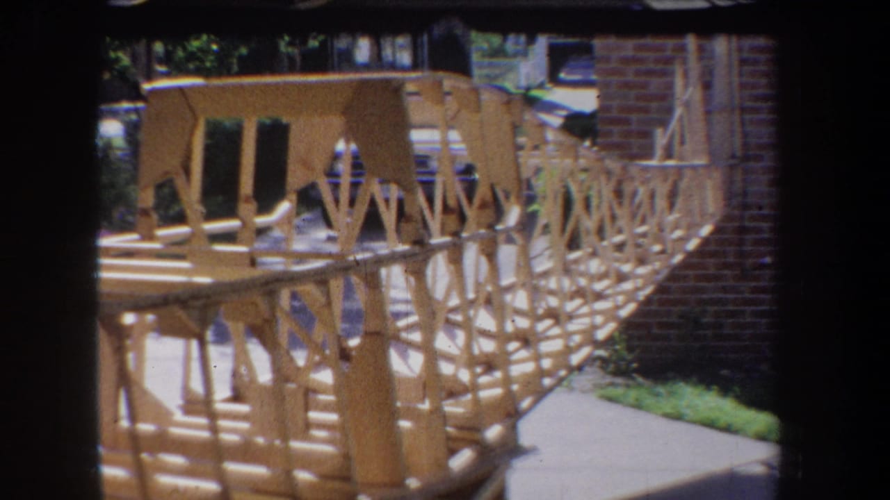 Large wooden truss-like model structure outdoors near a brick wall.
