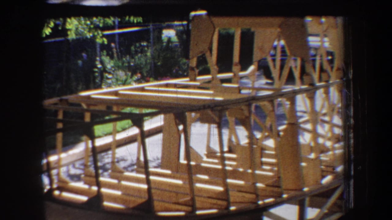 1965 8mm frame from Yucaipa, California showing a wooden boat skeleton under construction in a residential yard.