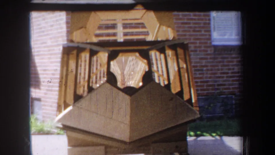 1965 Yucaipa-area 8mm frame showing the wooden sculpture from a slightly lower handheld angle outside a brick building.