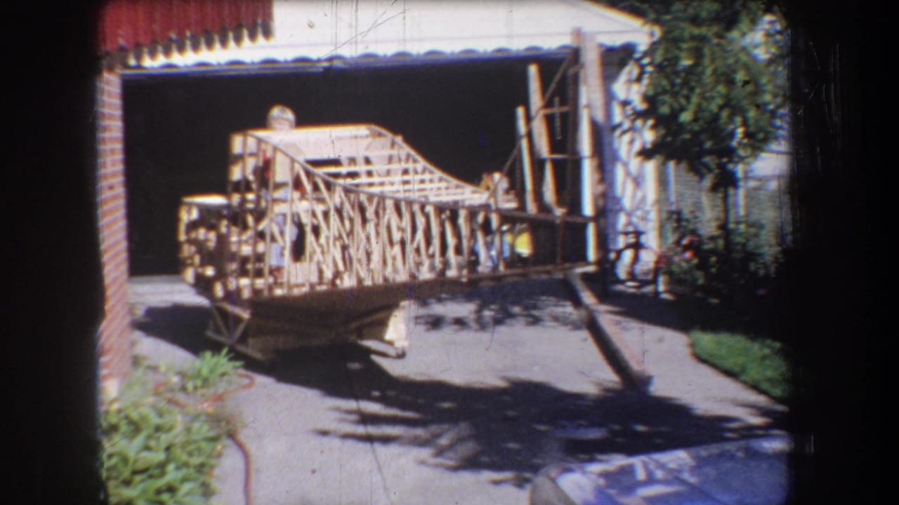 1965 Yucaipa-area home-movie frame showing a large handmade wooden structure on a driveway beside a garage.