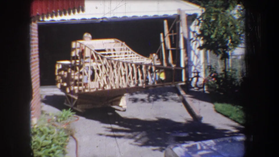 1965 Yucaipa-area home-movie frame showing a large handmade wooden structure on a driveway beside a garage.