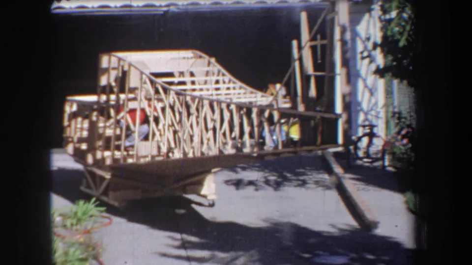 1965 Yucaipa-area frame showing a boy crouching inside a large handmade wooden model beside a garage.