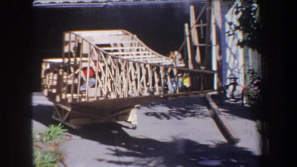 1965 Volmer Yucaipa home-movie frame with a boy inside the wooden framed model in a residential driveway.