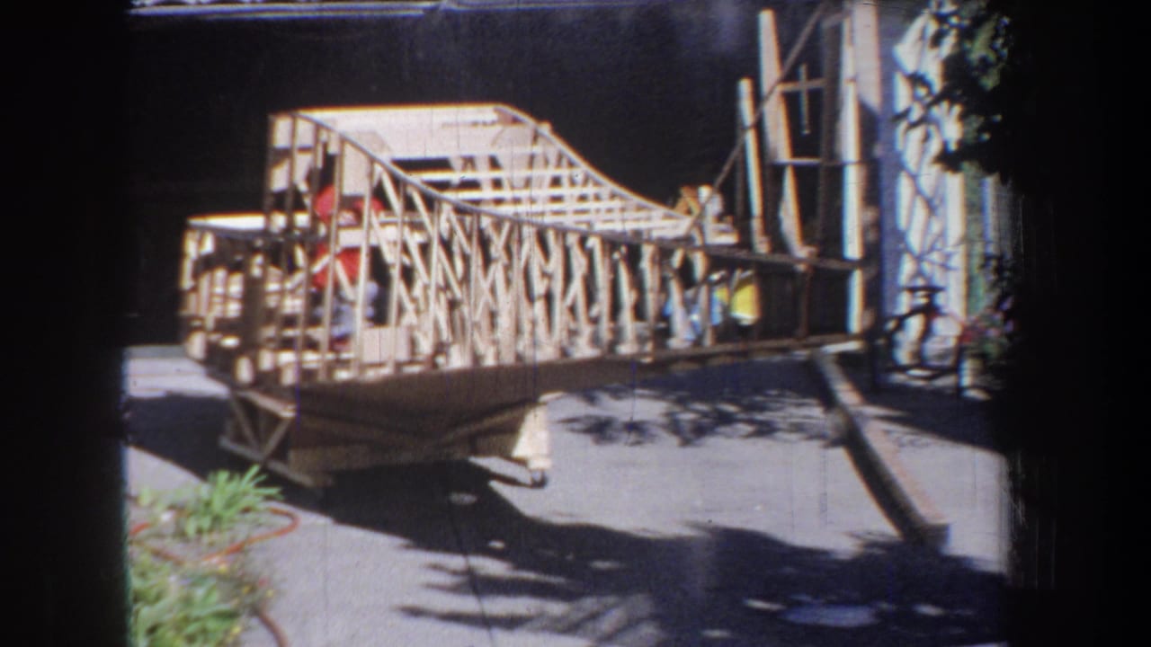 The home-built airplane frame appears from the side, with exposed ribs and a person partly visible near the fuselage.