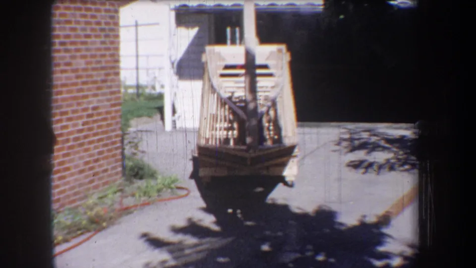 Rear-facing view of the unfinished wooden airplane structure on a residential driveway in the 1965 Yucaipa footage.