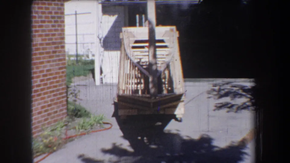 The final frame holds on the unfinished home-built airplane from behind, with the driveway, brick wall, and house exterior visible.