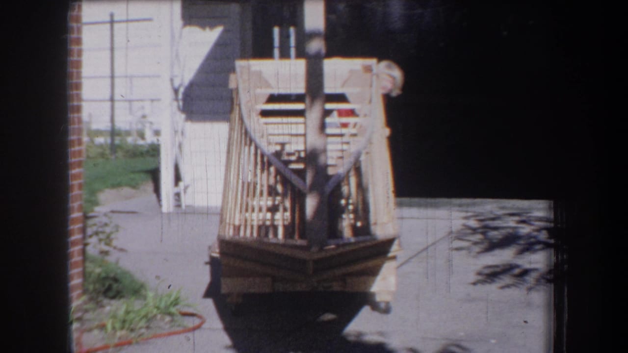 1965 Yucaipa-area home-movie frame showing a handmade wooden toy vehicle on a sunny residential driveway.
