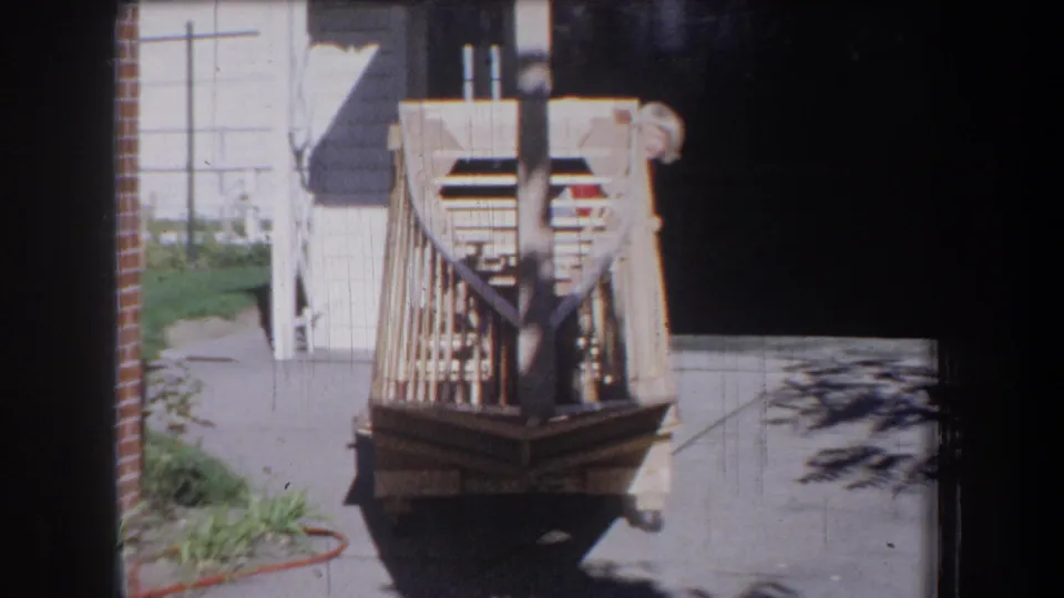 1965 Yucaipa-area home-movie frame showing a handmade wooden toy vehicle on a sunny residential driveway.
