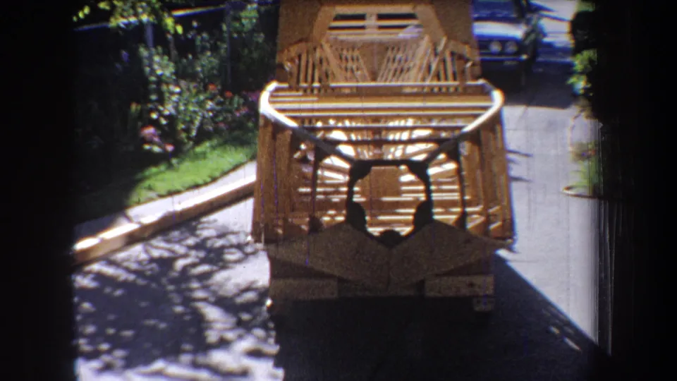 Small-gauge film frame from 1965 showing a handmade wooden toy vehicle on a residential driveway in Yucaipa-area California.